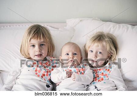 Stock Photography - Sisters in matching shirts laying on bed. Fotosearch