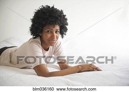 Stock Image - Smiling Black woman laying on bed. Fotosearch