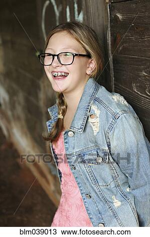 Stock Image - Smiling Caucasian girl leaning on wooden wall. Fotosearch