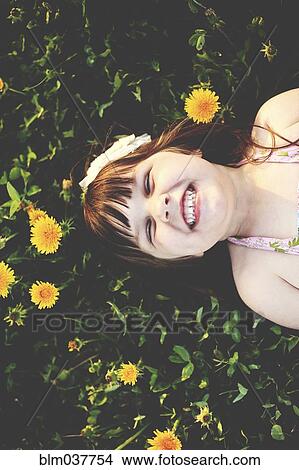 Picture - Smiling girl laying in grass with flowers. Fotosearch