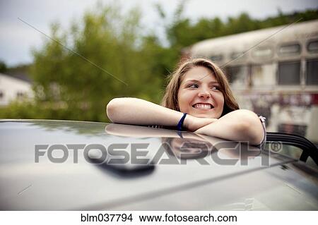 Picture - Smiling girl leaning on car roof. Fotosearch
