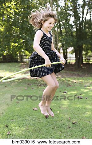 Stock Photograph - Smiling girl playing with plastic hoop in field. Fotosearch