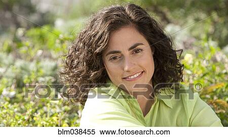 Stock Photography - Smiling Hispanic woman sitting in garden. Fotosearch