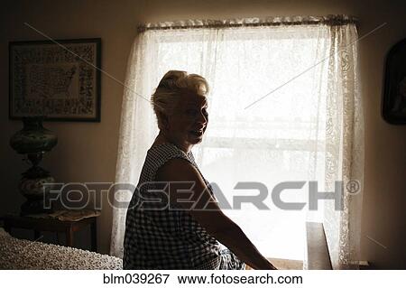 Stock Photo - Smiling older woman sitting on bed. Fotosearch