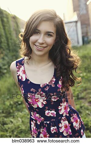 Stock Image - Smiling teenage girl standing in overgrown garden. Fotosearch