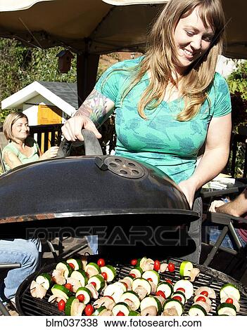 Stock Photo - Smiling woman grilling kebabs in backyard. Fotosearch