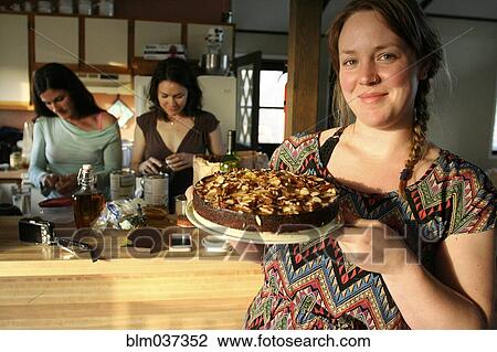 Stock Image - Smiling woman holding cake in kitchen. Fotosearch