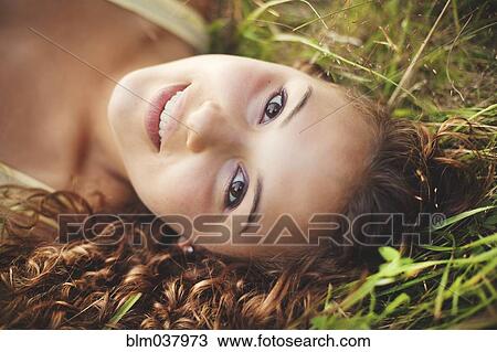 Stock Image - Smiling woman laying in grass. Fotosearch