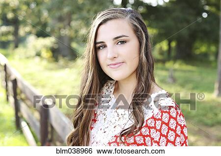 Stock Photograph - Smiling woman standing at wooden fence in rural field. Fotosearch