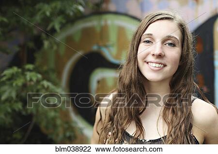 Stock Image - Smiling woman standing near graffiti wall. Fotosearch