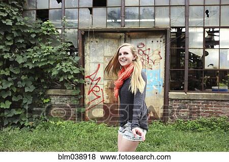 Stock Photo - Smiling woman walking outside dilapidated building. Fotosearch