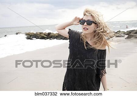 Stock Image - Smiling woman wearing sunglasses on beach. Fotosearch