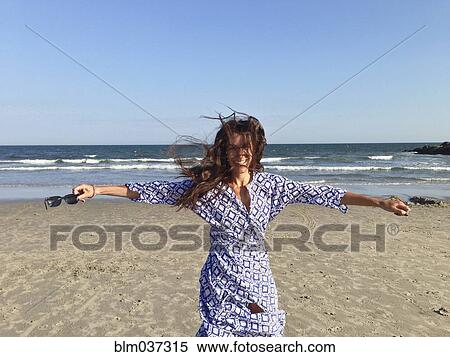 Stock Photography - Smiling woman with arms outstretched on beach. Fotosearch
