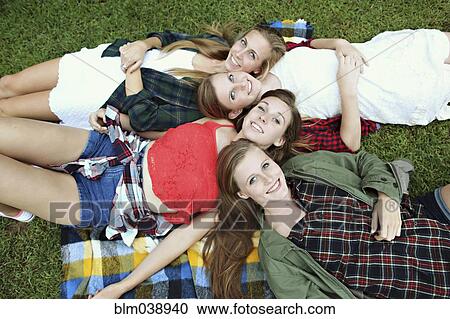 Stock Image - Smiling women laying on blanket in grass. Fotosearch