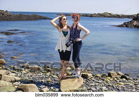 Stock Photo - Smiling women standing on rocky beach. Fotosearch