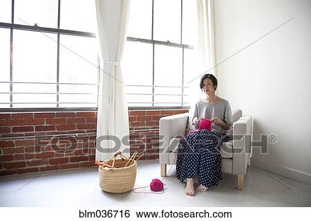 Stock Photograph - Taiwanese woman knitting in armchair near window. Fotosearch