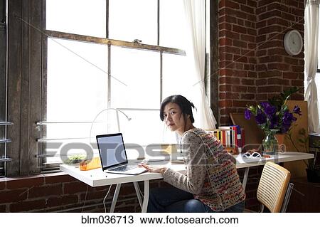 Stock Image - Taiwanese woman using laptop in home office. Fotosearch