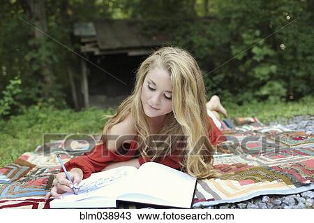 Stock Image - Teenage girl drawing in notebook on blanket. Fotosearch
