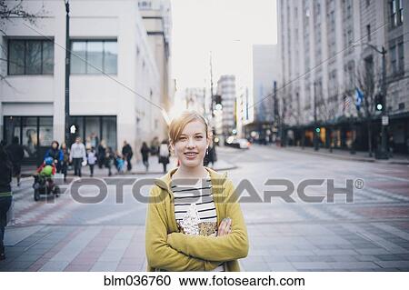 Stock Image - Teenage girl standing with arms crossed in city intersection. Fotosearch