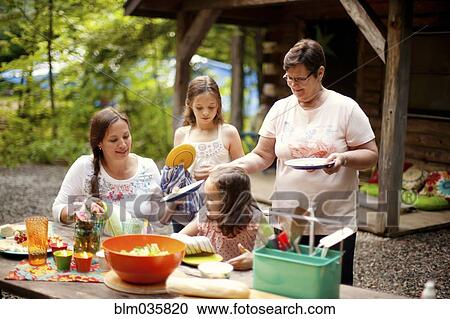 Stock Image - Three generations of Caucasian women cooking outside cabin. Fotosearch
