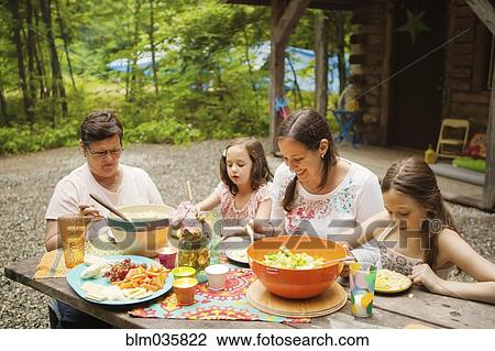 Stock Image - Three generations of Caucasian women eating outside cabin. Fotosearch