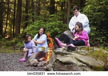 Stock Image - Three generations of Caucasian women sitting around campfire. Fotosearch