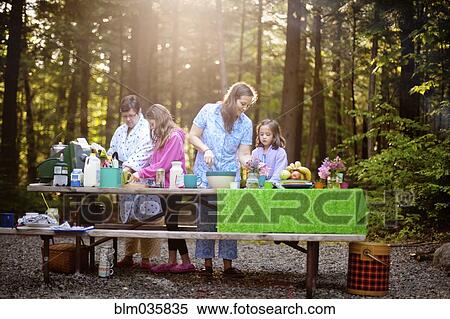 Stock Photography - Three generations of Caucasian women cooking at picnic table. Fotosearch