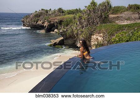 Stock Image - Woman admiring beach view from swimming pool. Fotosearch
