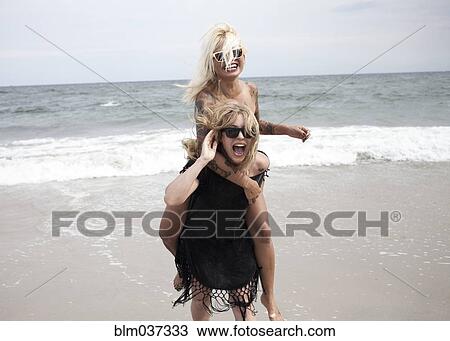 Woman carrying friend piggyback on beach View Large Photo Image Stock Image - Woman carrying friend piggyback on beach. Fotosearch