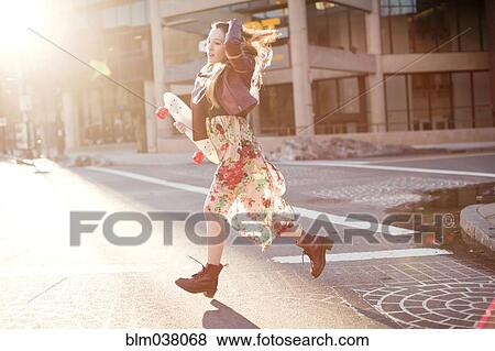 Stock Photo - Woman carrying skateboard in city intersection. Fotosearch
