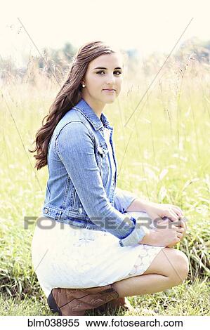 Stock Photography - Woman crouching in tall grass in field. Fotosearch