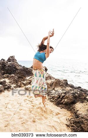 Stock Image - Woman dancing on rocky beach. Fotosearch