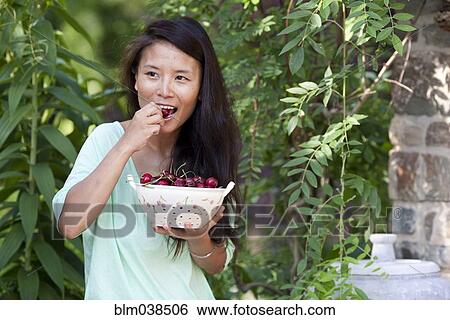 Stock Photograph - Woman eating grapes in garden. Fotosearch