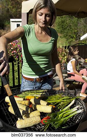 Stock Photograph - Woman grilling vegetables on patio. Fotosearch