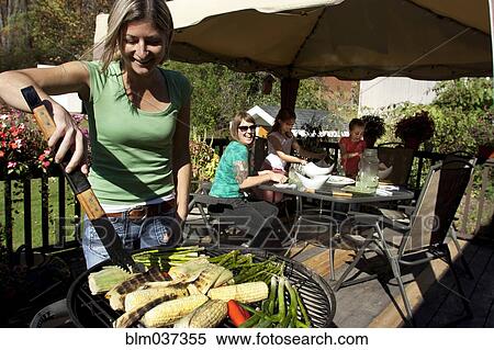 Stock Photography - Woman grilling vegetables on patio. Fotosearch