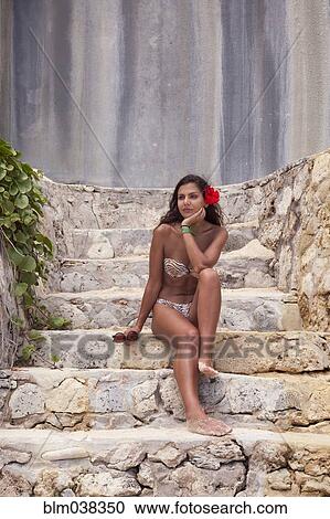 Stock Image - Woman in bikini sitting on stone steps. Fotosearch
