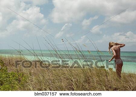 Stock Photo - Woman in bikini standing in beach grass. Fotosearch