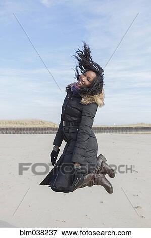 Woman in coat jumping for joy on beach View Large Photo Image Stock Photo - Woman in coat jumping for joy on beach. Fotosearch