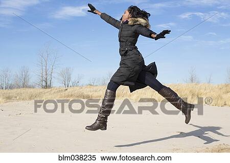 Woman in coat jumping for joy on beach View Large Photo Image Stock Photography - Woman in coat jumping for joy on beach. Fotosearch