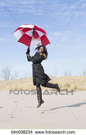 Picture - Woman in coat playing with umbrella on beach. Fotosearch