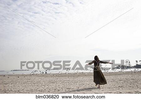 Stock Image - Woman in dress playing on beach. Fotosearch