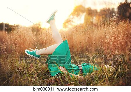 Stock Image - Woman laying in tall grass and kicking. Fotosearch