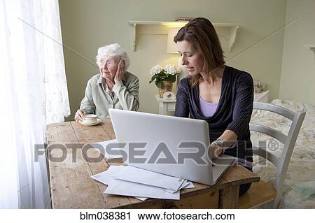 Stock Image - Woman paying bills for elderly mother. Fotosearch