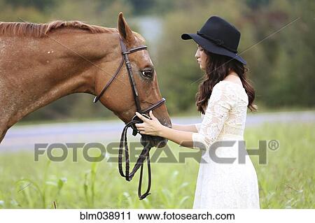 Stock Image - Woman petting horse in rural field. Fotosearch