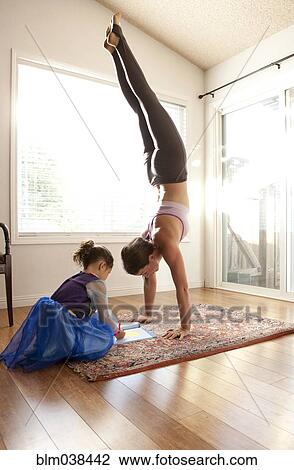 Stock Image - Woman practicing yoga and helping daughter with homework. Fotosearch