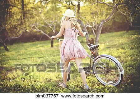 Stock Photo - Woman pushing bicycle in rural field. Fotosearch