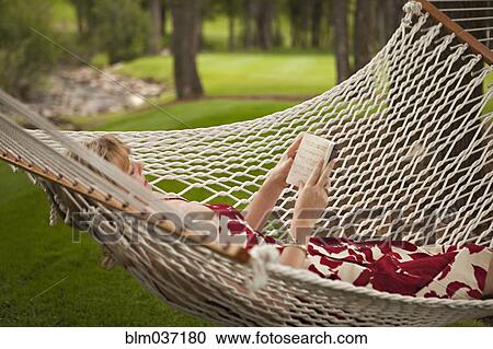 Stock Image - Woman reading book in backyard hammock. Fotosearch