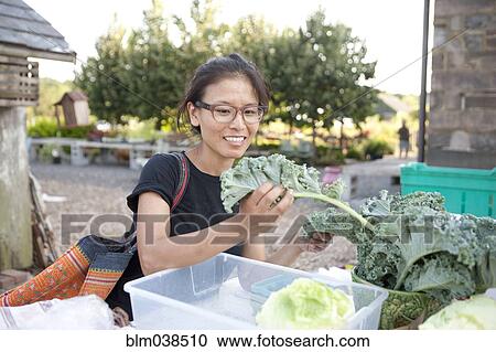 Stock Image - Woman shopping for greens at farmers market. Fotosearch