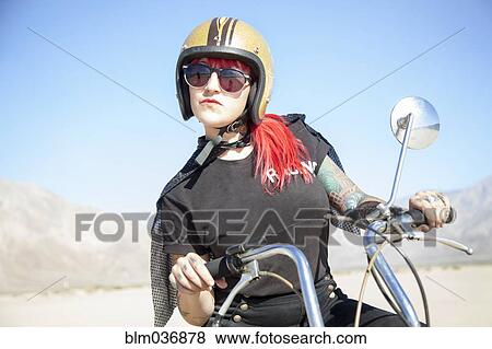 Stock Photo - Woman sitting on motorcycle in desert. Fotosearch