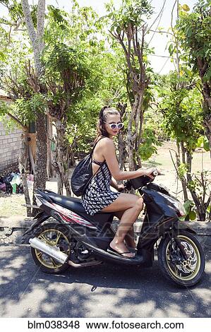 Stock Photo - Woman sitting on scooter near trees. Fotosearch